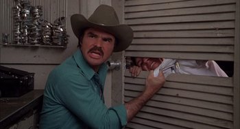 Movie still from “Smokey and the Bandit II” (1980), directed by Hal Needham – A man in a cowboy hat is holding a newspaper; Medium shot, Low angle