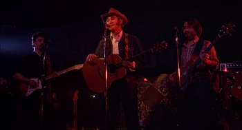 Movie still from “Smokey and the Bandit II” (1980), directed by Hal Needham – A man in a cowboy hat playing a guitar on a stage; Medium shot, Low angle