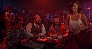 Movie still from “Smokey and the Bandit II” (1980), directed by Hal Needham – A group of men sitting at a table in front of a crowd; Wide shot, Over the shoulder angle