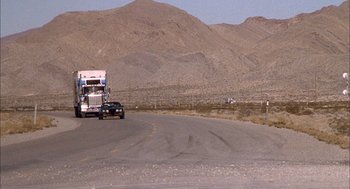 Movie still from “Smokey and the Bandit II” (1980), directed by Hal Needham – A truck driving down a road near a mountain range; Extreme Wide shot, High angle