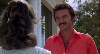 Movie still from “Smokey and the Bandit II” (1980), directed by Hal Needham – A person wearing a red shirt near a building; Close Up shot, Over the shoulder angle