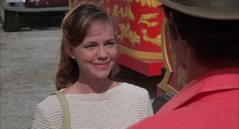 Movie still from “Smokey and the Bandit II” (1980), directed by Hal Needham – A young woman smiles at the camera while standing next to a man; Close Up shot, Over the shoulder angle