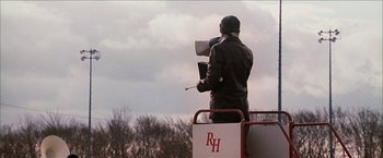 Movie still from “Snow Angels” (2007), directed by David Gordon Green – A man standing on top of a truck holding a microphone; Wide shot, Low angle