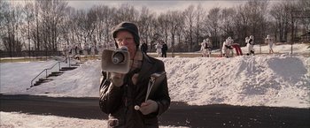 Movie still from “Snow Angels” (2007), directed by David Gordon Green – An older woman holding a microphone and a pair of skis; Medium shot, Low angle