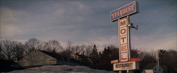 Movie still from “Snow Angels” (2007), directed by David Gordon Green – A motel sign in front of trees in the snow; Wide shot, Low angle