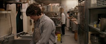 Movie still from “Snow Angels” (2007), directed by David Gordon Green – A group of people in a kitchen preparing food; Medium shot, Over the shoulder angle