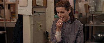 Movie still from “Snow Angels” (2007), directed by David Gordon Green – A woman is eating something while standing in front of a wall; Close Up shot, Over the shoulder angle