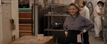 Movie still from “Snow Angels” (2007), directed by David Gordon Green – A woman standing in front of a table in a kitchen; Medium shot, Over the shoulder angle