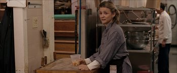 Movie still from “Snow Angels” (2007), directed by David Gordon Green – A woman sitting at a table holding a container of food; Medium shot, Over the shoulder angle