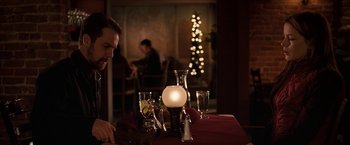 Movie still from “Snow Angels” (2007), directed by David Gordon Green – A man sitting at a table with a lit candle in the middle; Medium shot, Over the shoulder angle