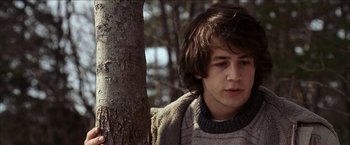 Movie still from “Snow Angels” (2007), directed by David Gordon Green – A young man leaning against a tree in a wooded area; Close Up shot, Low angle