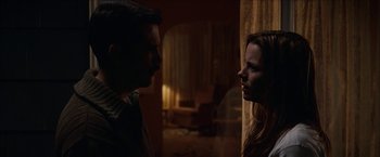 Movie still from “Snow Angels” (2007), directed by David Gordon Green – A man and a woman standing next to each other in a dark room; Medium shot, Low angle