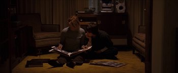 Movie still from “Snow Angels” (2007), directed by David Gordon Green – Two people sitting on the floor looking at a magazine; Wide shot, High angle