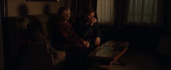 Movie still from “Snow Angels” (2007), directed by David Gordon Green – A man and a woman sitting in a living room next to a coffee table; Medium shot, High angle