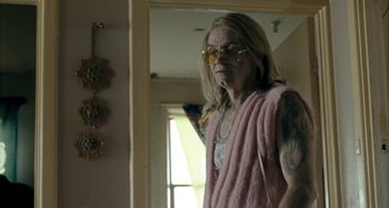 Movie still from “The Snowtown Murders” (2011), directed by Justin Kurzel – An older woman wearing a pink robe and yellow glasses; Medium shot, Over the shoulder angle