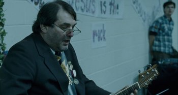 Movie still from “The Snowtown Murders” (2011), directed by Justin Kurzel – A man in a suit and tie holding a guitar; Close Up shot, Over the shoulder angle