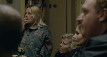 Movie still from “The Snowtown Murders” (2011), directed by Justin Kurzel – A group of people sitting in a living room smoking; Medium shot, Over the shoulder angle