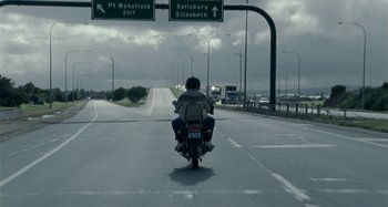 Movie still from “The Snowtown Murders” (2011), directed by Justin Kurzel – A man riding a motorcycle down the middle of the road; Extreme Wide shot, Low angle