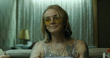 Movie still from “The Snowtown Murders” (2011), directed by Justin Kurzel – A man with long blonde hair and tattoos wearing yellow glasses; Close Up shot, Over the shoulder angle