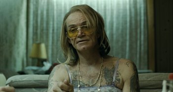 Movie still from “The Snowtown Murders” (2011), directed by Justin Kurzel – A person with tattoos and glasses sitting in a room; Close Up shot, Over the shoulder angle