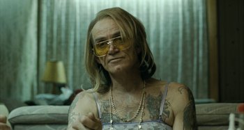 Movie still from “The Snowtown Murders” (2011), directed by Justin Kurzel – A man with long blonde hair and tattoos wearing sunglasses; Close Up shot, Over the shoulder angle