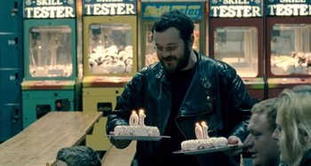 Movie still from “The Snowtown Murders” (2011), directed by Justin Kurzel – A man in a leather jacket holding two cakes with lit candles on them; Medium shot, Over the shoulder angle