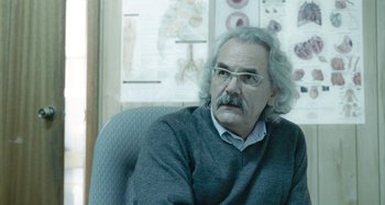 Movie still from “The Snowtown Murders” (2011), directed by Justin Kurzel – An older man sitting in a chair in a room; Close Up shot, Over the shoulder angle