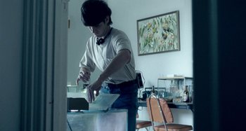 Movie still from “The Snowtown Murders” (2011), directed by Justin Kurzel – A man in white shirt and blue jeans cutting paper; Medium shot, Low angle