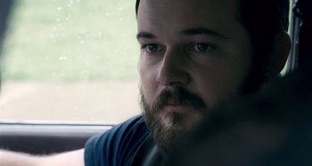 Movie still from “The Snowtown Murders” (2011), directed by Justin Kurzel – A person with a beard looking out a window; Close Up shot, Over the shoulder angle