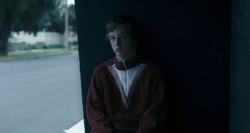 Movie still from “The Snowtown Murders” (2011), directed by Justin Kurzel – A young boy is sitting against a wall; Medium shot, Over the shoulder angle