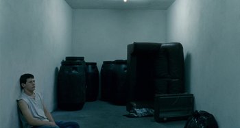 Movie still from “The Snowtown Murders” (2011), directed by Justin Kurzel – A room filled with furniture and large black containers; Wide shot, High angle