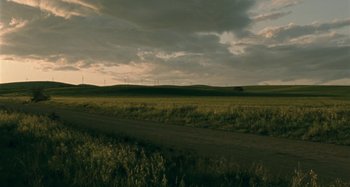 Movie still from “The Snowtown Murders” (2011), directed by Justin Kurzel – A dirt road running through a green field with a cloudy sky in the background; Extreme Wide shot, High angle