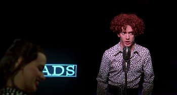 Movie still from “So I Married an Axe Murderer” (1993), directed by Thomas Schlamme – A man with red hair is singing into a microphone; Medium shot, Over the shoulder angle