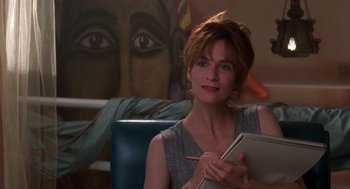 Movie still from “So I Married an Axe Murderer” (1993), directed by Thomas Schlamme – A woman sitting in front of a painting holding a notebook; Close Up shot, Over the shoulder angle