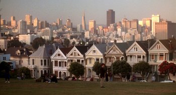 Movie still from “So I Married an Axe Murderer” (1993), directed by Thomas Schlamme – A group of people sitting on top of a grass covered field; Extreme Wide shot, High angle