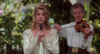 Movie still from “So I Married an Axe Murderer” (1993), directed by Thomas Schlamme – A woman holding a microphone in front of a man with a violin; Medium shot, Over the shoulder angle