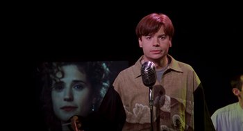 Movie still from “So I Married an Axe Murderer” (1993), directed by Thomas Schlamme – A man standing next to a microphone in front of a picture of a woman; Close Up shot, Low angle