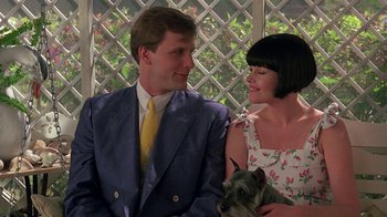 Movie still from “Something Wild” (1986), directed by Jonathan Demme – A man and a woman sitting next to each other holding a dog; Medium shot, Low angle