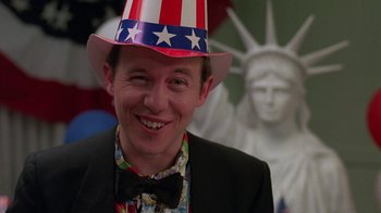 Movie still from “Something Wild” (1986), directed by Jonathan Demme – A man wearing a patriotic hat in front of the statue of liberty; Close Up shot, Low angle