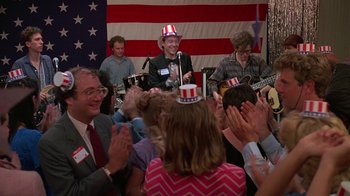 Movie still from “Something Wild” (1986), directed by Jonathan Demme – A group of people sitting in front of an american flag; Medium shot, High angle