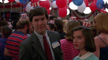 Movie still from “Something Wild” (1986), directed by Jonathan Demme – A man and a woman wearing patriotic hats in front of a crowd; Close Up shot, Over the shoulder angle
