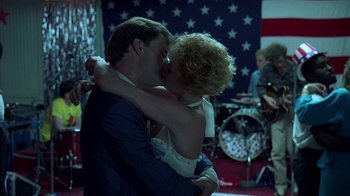 Movie still from “Something Wild” (1986), directed by Jonathan Demme – A man and a woman kissing in front of an american flag; Medium shot, Low angle