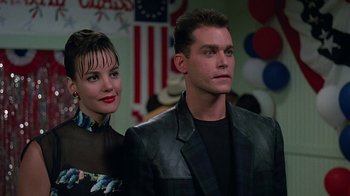Movie still from “Something Wild” (1986), directed by Jonathan Demme – A man and a woman standing next to each other in front of american flags; Close Up shot, Over the shoulder angle