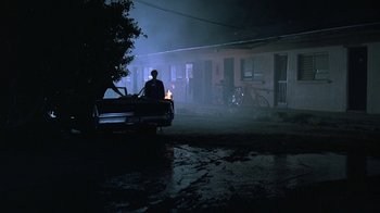 Movie still from “Something Wild” (1986), directed by Jonathan Demme – A man sitting on the hood of a car at night; Wide shot, Low angle