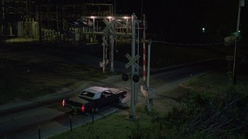 Movie still from “Something Wild” (1986), directed by Jonathan Demme – A car is stopped at a railroad crossing at night; Extreme Wide shot, High angle