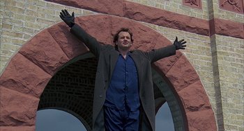 Movie still from “Groundhog Day” (1993), directed by Harold Ramis – A man standing in front of an archway with his arms outstretched; Wide shot, Low angle