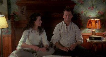 Movie still from “Groundhog Day” (1993), directed by Harold Ramis – A man and a woman sitting on a couch in front of a fire place; Medium shot, Over the shoulder angle