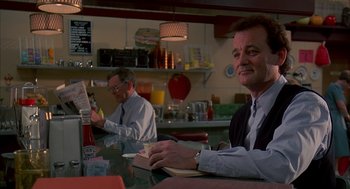 Movie still from “Groundhog Day” (1993), directed by Harold Ramis – A man sitting at a table in front of another man; Medium shot, Over the shoulder angle