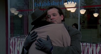 Movie still from “Groundhog Day” (1993), directed by Harold Ramis – A man hugging another man in front of a building; Medium shot, Over the shoulder angle