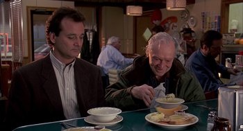 Movie still from “Groundhog Day” (1993), directed by Harold Ramis – Two men sitting at a table with bowls of food; Medium shot, Over the shoulder angle